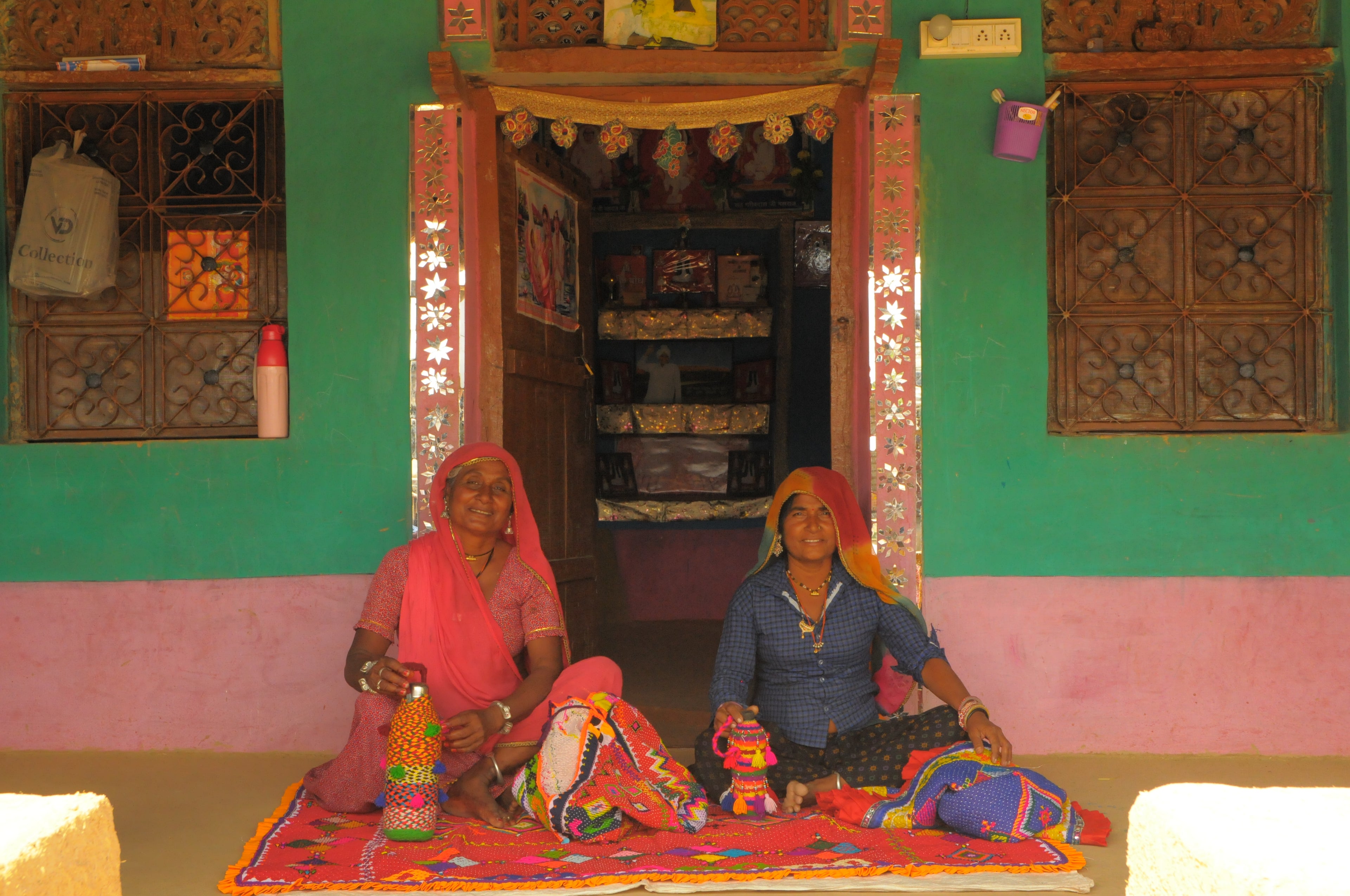 Two women sitting on a colorful rug in a room with green walls and wooden furniture.